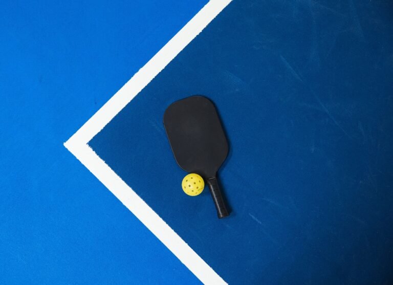 Close-up of a pickleball paddle and ball on a vibrant blue court surface showing geometric lines.