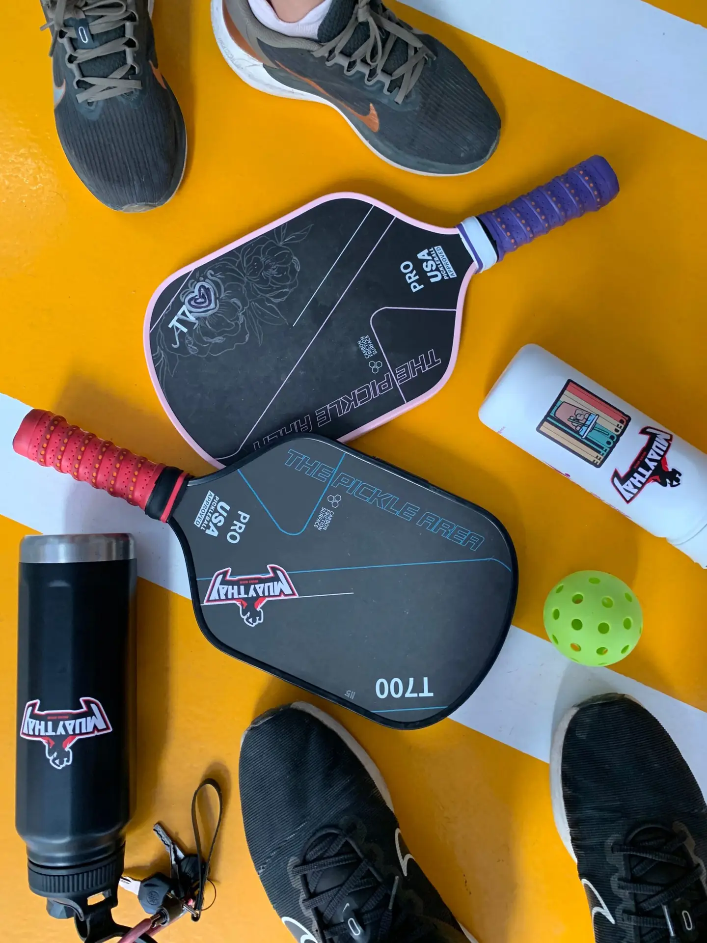 Flat lay of pickleball paddles, ball, and shoes on a court, featuring sports gear.